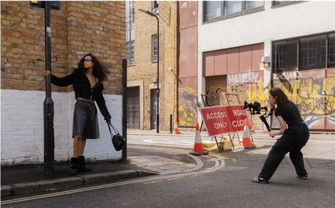 Behind-the-scenes campaign shoot in an urban setting, with a videographer filming a BUFFALO model posing on a city street location.