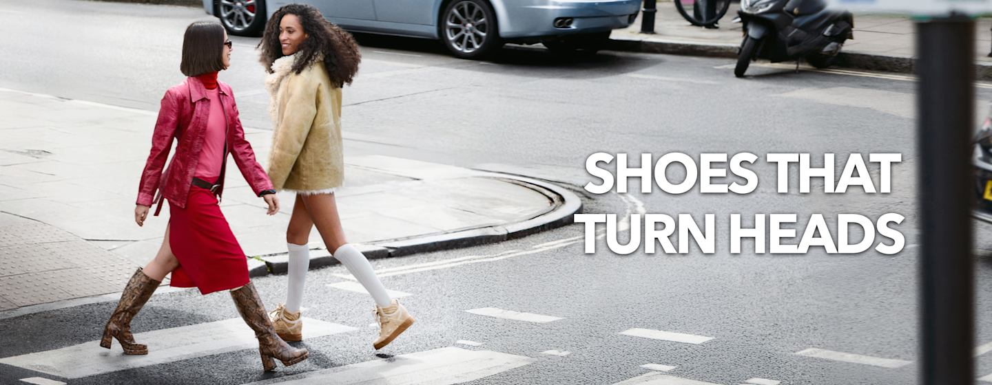 Two people crossing a city street wearing statement boots and sneakers, featured alongside promotional campaign text.