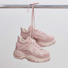 Pink chunky sneakers hanging by their laces from a metal rail against a light background.
