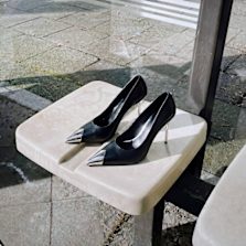 Black high-heel pumps with metallic toe caps placed on a stone bench in an outdoor setting.