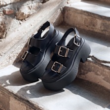 Black chunky platform sandals with buckle straps placed on stone steps in natural light