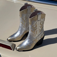 Metallic cowboy‑style ankle boots with decorative stitching placed on a car trunk.