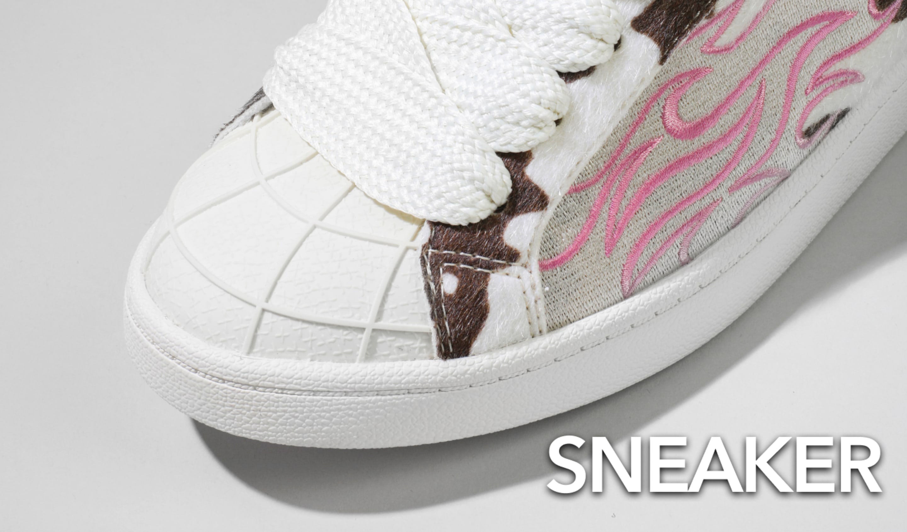Close-up of a white sneaker with oversized laces, textured toe cap, and pink flame embroidery, alongside the text “SNEAKER”.