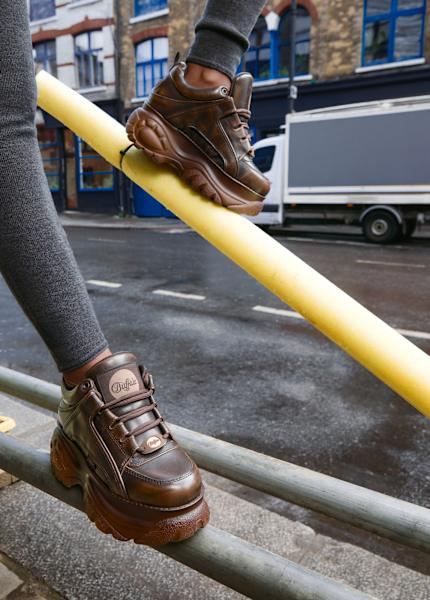 Close-up of brown Buffalo platform sneakers balanced on urban railings in a city street setting.